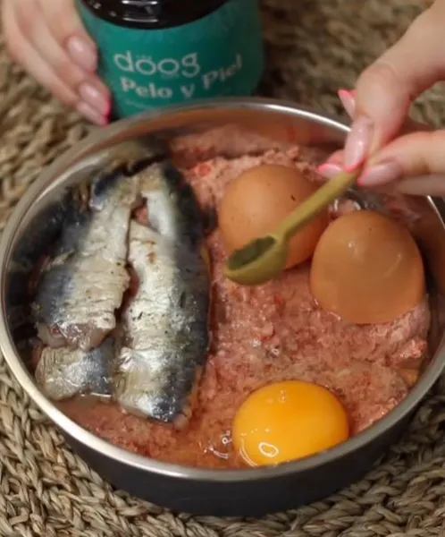 Comida natural para perros con sardinas, carne cruda, huevos y suplemento nutricional para mejorar la salud del pelo y la piel.