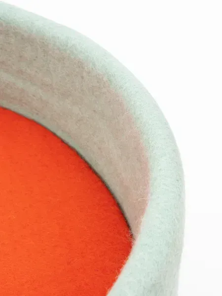 Detalle de cama para perros hecha a mano y sostenible en fieltro azul cielo con interior rojo anaranjado, mostrando la textura natural y suave del material.