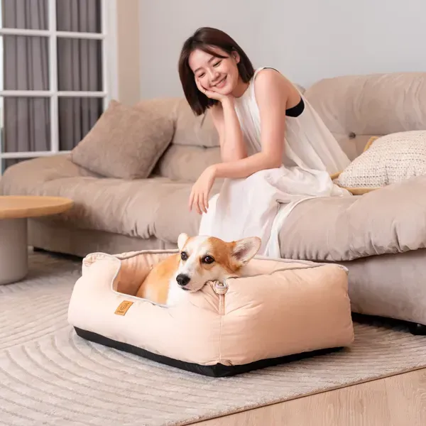 Perro Corgi relajado en una cama ortopédica para perros de color beige, junto a su humana en una sala confortable.