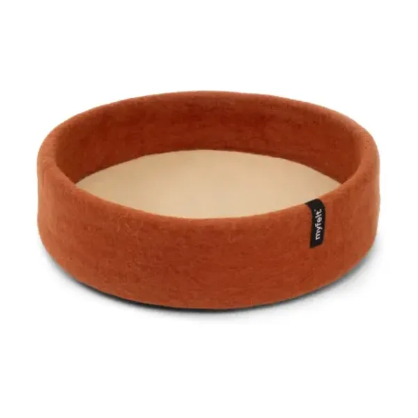 Cesta redonda para perros hecha a mano con fieltro de lana virgen. Diseño sostenible en color terracota con base beige, proporcionando comodidad y aislamiento térmico. Etiqueta de la marca myfelt en el lateral.